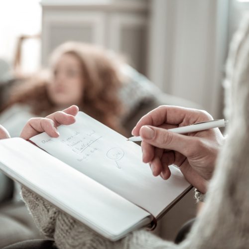 Making notes. Close up of professional psychologist making notes listening to stressed client